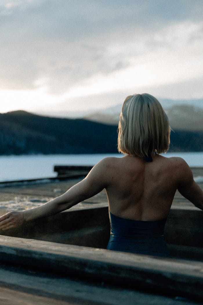 Blonde woman enjoying relaxation in an outdoor hot tub with a scenic mountain backdrop at sunset.